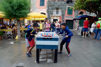 SYDNEY DELBRIDGE, MANAROLA, CINQUE TERRE, ITALY: Kids partake  in an intense game of foosball as tourists watch.